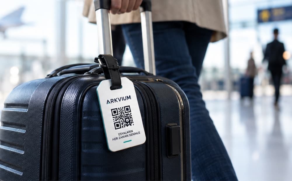 Havalimanında çekilen lacivert valiz ve sapına takılı QR kodlu ARKVIUM valiz etiketi